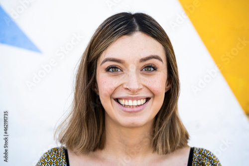 Woman with brown eyes smiling in front of wall photo