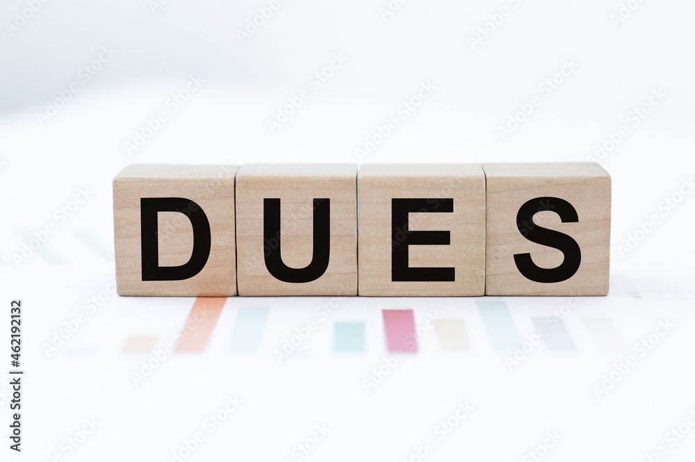 Word Dues on wooden cubes on a background of colored financial charts Word Dues on wooden cubes on a background of colored financial charts
