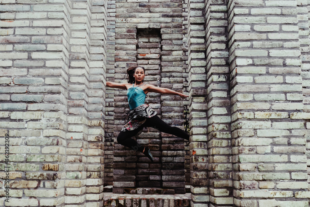 Young woman with arms outstretched jumping in front of stone wall Young woman with arms outstretched jumping in front of stone wall