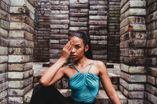 Young female dancer covering eye while sitting in front of stone structure photo