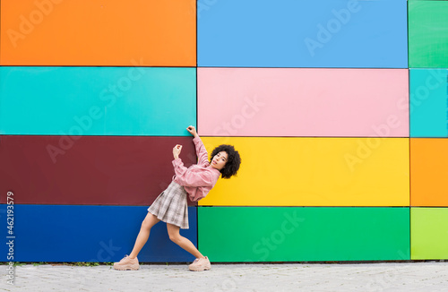 Young woman bending over backwards while standing by multi colored wall