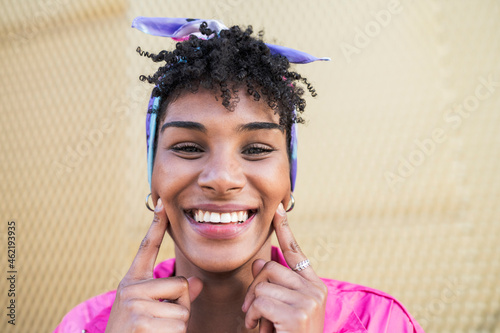 Smiling young woman touching cheeks with index fingers