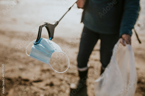 Beach cleanup volunteer picking up face mask for environment campaign photo