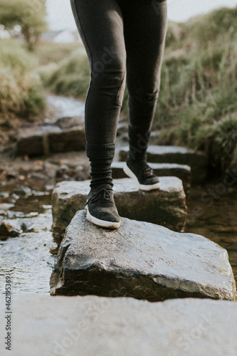 Woman on adventure crossing the stream by stepping stone