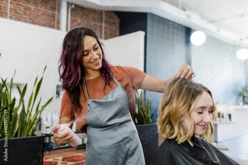 Obraz Hairstylist spraying a mouse on her customer's hair
