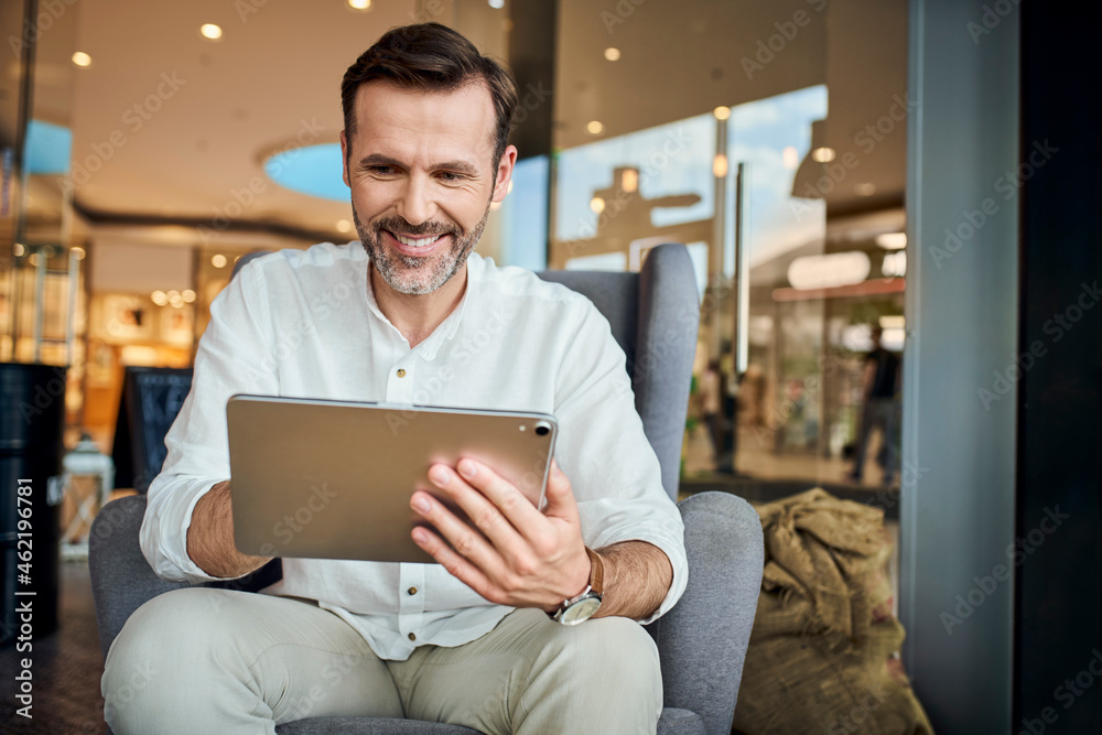 Happy man in cafe using digital tablet sitting on armchair