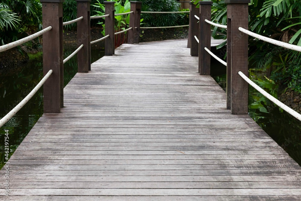 A dark wooden bridge crosses a pond in a tropical garden