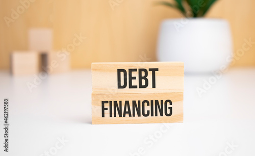 On a light background, wooden cubes and a wooden block with the text Debt financing. View from above