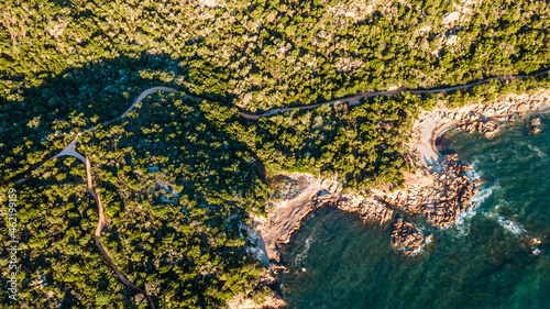 early in the morning, sunrise on an island in the mediterranean sea. warm light, paths leading to the bay, many green bushes and plants. soft blue water, waves breaking in the reef. drone, aerial view