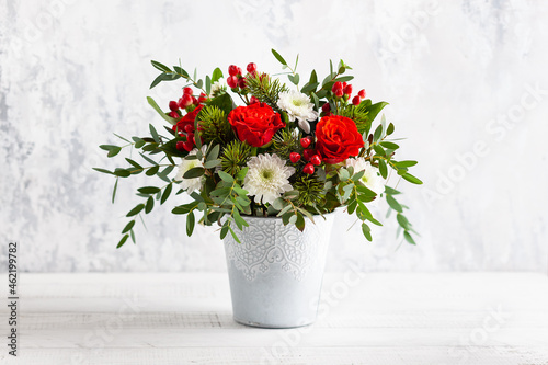 Festive winter flower arrangement with red roses, white chrysanthemum and berries in vase on table. Christmas flower composition for holiday. © Svetlana Kolpakova