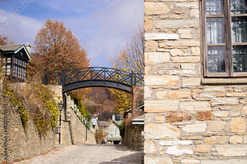 Black metal suspension bridge on an autumn street in Nymfaio Greece. Wrought iron grates, wooden frames in a stone house in the foreground photo