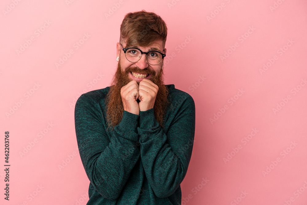 Young caucasian ginger man with long beard isolated on pink background keeps hands under chin, is looking happily aside. Young caucasian ginger man with long beard isolated on pink background keeps hands under chin, is looking happily aside.