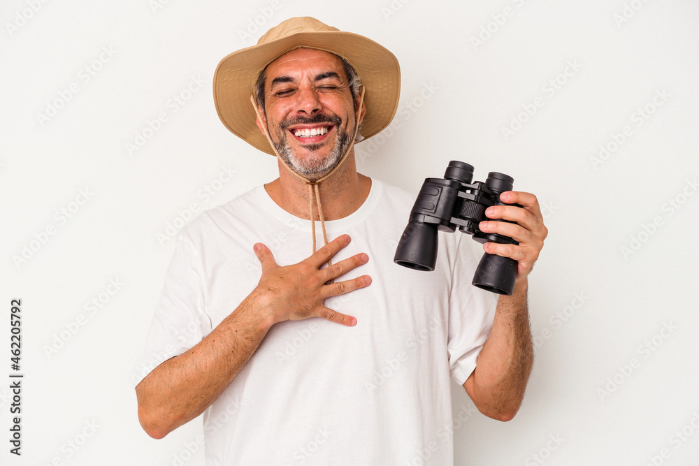 Middle age caucasian man holding binoculars isolated on white background laughs out loudly keeping hand on chest. Middle age caucasian man holding binoculars isolated on white background laughs out loudly keeping hand on chest.