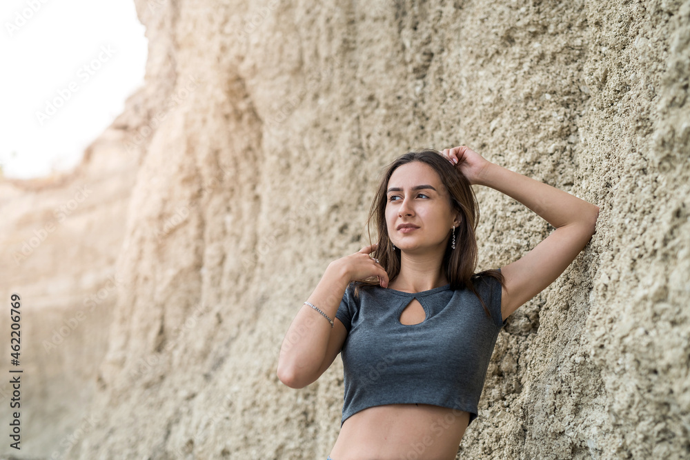 slim sporty girl in a casual clothes posing against the rocks of sand in quarry