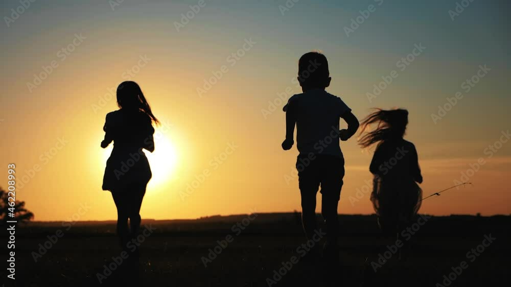 Happy young mother with a children play together on park. Silhouette of happy people running at sunset in the park. Happy parents childhood dream concept. Happy young mother with a children play together on park. Silhouette of happy people running at sunset in the park. Happy parents childhood dream concept.