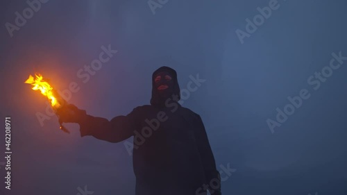 A man in a hood and balaclava holds a burning molotov cocktail in his hand photo