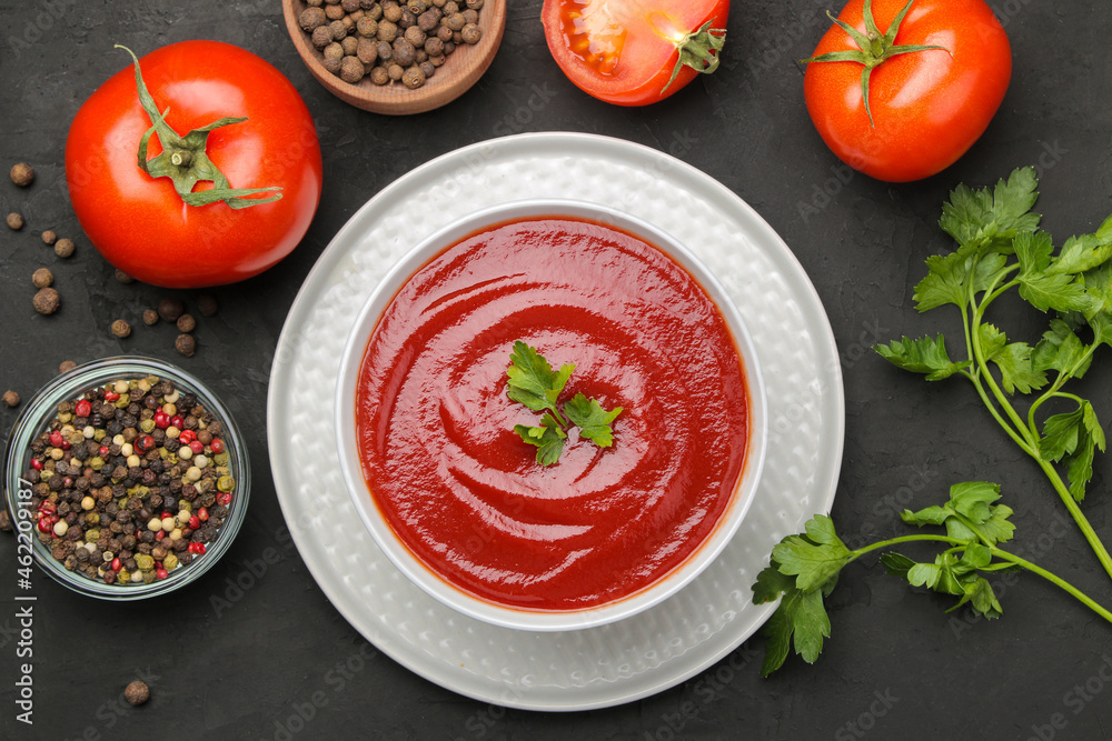 Delicious tomato soup on a black table and ingredients for cooking tomatoes and spices Delicious tomato soup on a black table and ingredients for cooking tomatoes and spices