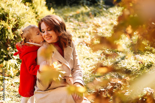 Autumn landscape. Happy mom and daughter, a child in a coat hugging together, walking and having fun in the fall forest on Mother's Day in nature outdoor. Selective focus