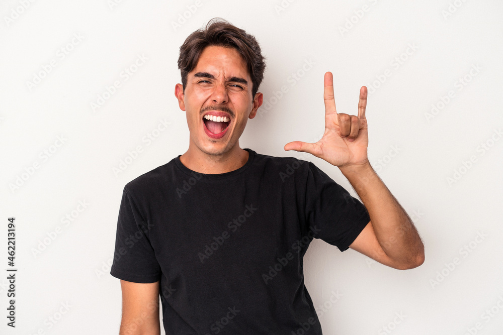 Young mixed race man isolated on white background showing a horns gesture as a revolution concept. Young mixed race man isolated on white background showing a horns gesture as a revolution concept.