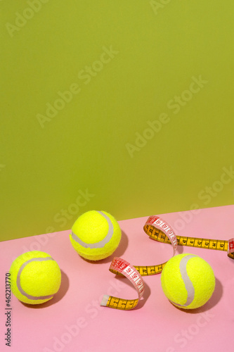 Vertical image of three tennis balls,measuring tape on the pink surface against green background.Empty space © uaPieceofCake