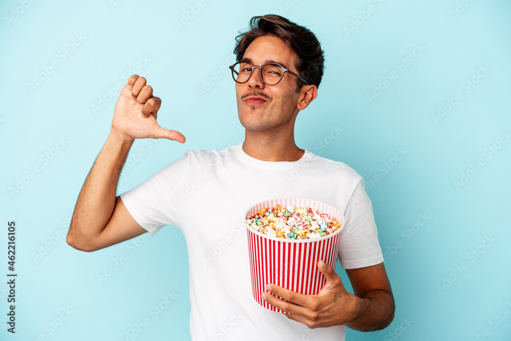Young mixed race man eating popcorns isolated on blue background feels proud and self confident, example to follow.