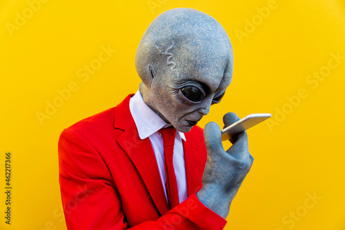 Portrait of man wearing alien costume and bright red suit using smart phone photo