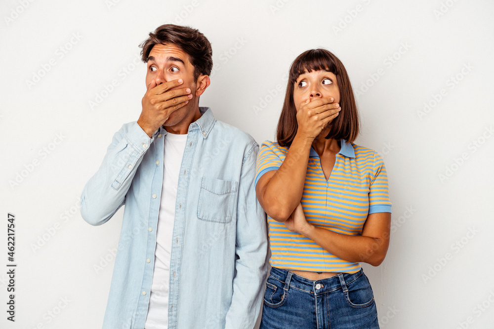 Young mixed race couple isolated on white background thoughtful looking to a copy space covering mouth with hand. Young mixed race couple isolated on white background thoughtful looking to a copy space covering mouth with hand.