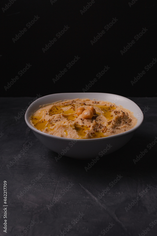 Chickpeas hummus with olive oil and toasted sesame on dark background and selective focus. 