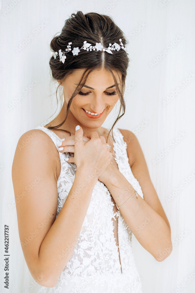 Tender portrait of the bride on a white background. A brunette with a delicate hairstyle and a white wreath poses in a white dress.