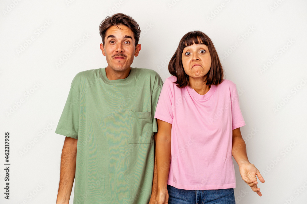 Young mixed race couple isolated on white background shrugs shoulders and open eyes confused. Young mixed race couple isolated on white background shrugs shoulders and open eyes confused.