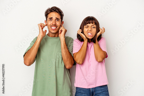 Young mixed race couple isolated on white background covering ears with fingers, stressed and desperate by a loudly ambient.