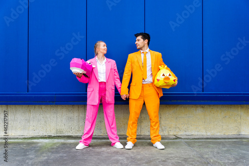 Man and woman wearing vibrant suits standing together in front of blue wall with animal masks in hands photo