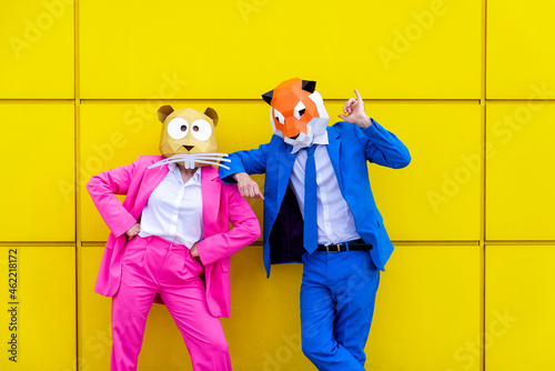 Man and woman wearing vibrant suits and animal masks posing together against yellow wall