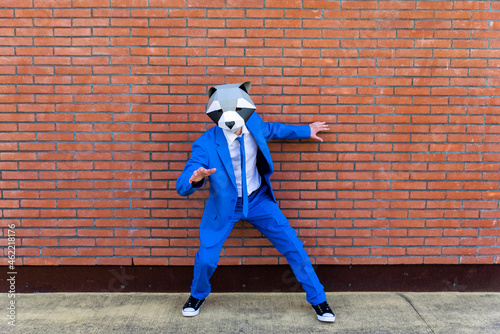 Man wearing vibrant blue suit and raccoon mask posing in front of brick wall photo