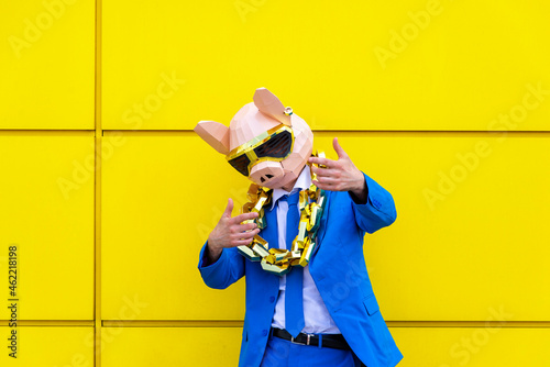 Man wearing vibrant blue suit, pig mask and large golden chain posing against yellow wall photo