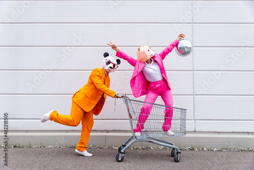 Man and woman wearing vibrant suits and animal masks messing around with shopping cart and disco ball photo