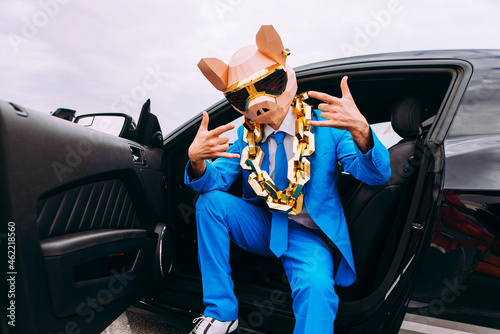 Funny character in animal mask and blue business suit sitting in car and gesturing