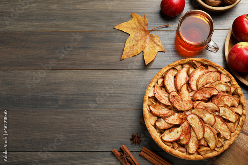 Delicious apple pie, ingredients and cup of tea on wooden table, flat lay. Space for text