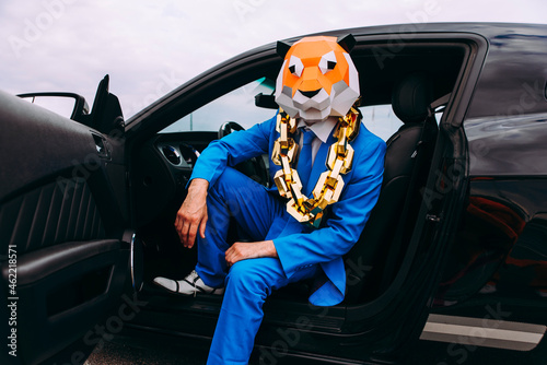 Funny character in animal mask and blue business suit sitting in car