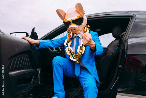 Funny character wearing animal mask and blue business suit showing middle finger from car