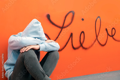 Sad teenage boy sitting in front German word for love on orange wall