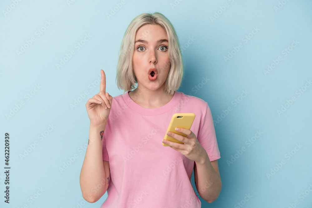 Young caucasian woman holding mobile phone isolated on blue background having some great idea, concept of creativity. Young caucasian woman holding mobile phone isolated on blue background having some great idea, concept of creativity.