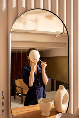 Reflection of woman applying lipstick on white mask photo