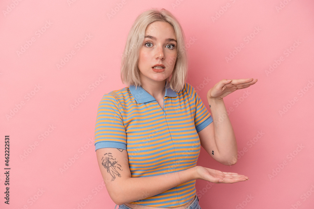Young caucasian woman isolated on pink background shocked and amazed holding a copy space between hands. Young caucasian woman isolated on pink background shocked and amazed holding a copy space between hands.