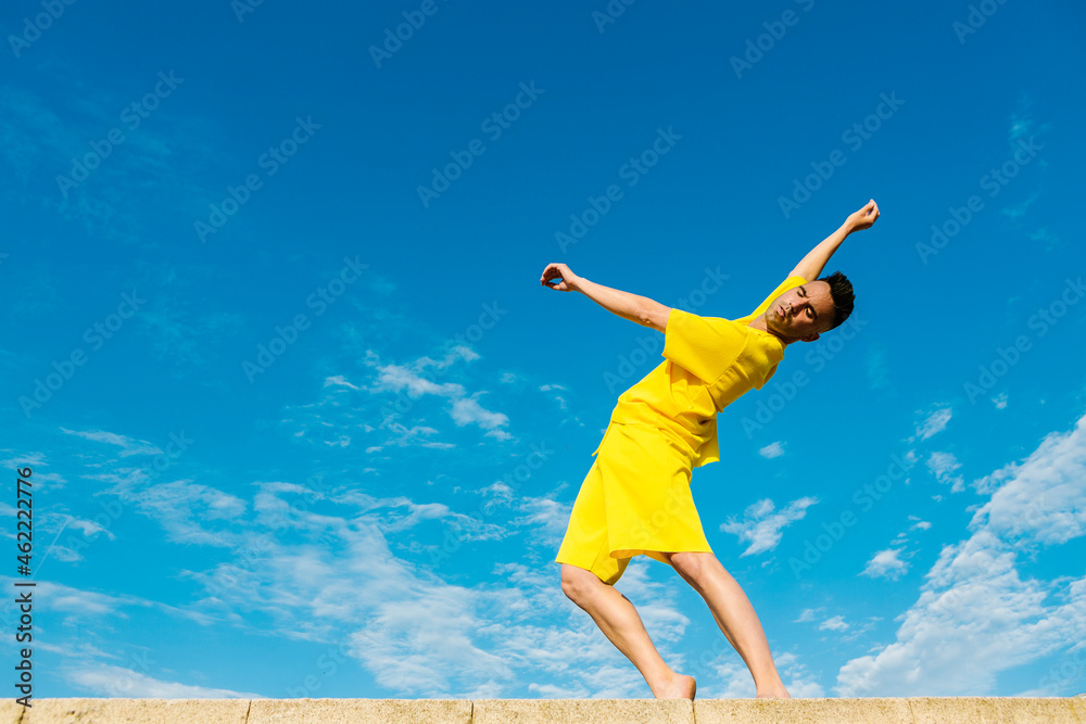 Young man dancing on retaining wall by blue sky Young man dancing on retaining wall by blue sky