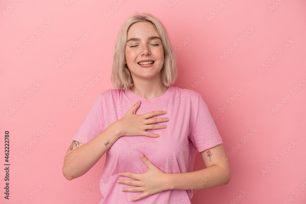 Young caucasian woman isolated on pink background laughs happily and has fun keeping hands on stomach. Young caucasian woman isolated on pink background laughs happily and has fun keeping hands on stomach.