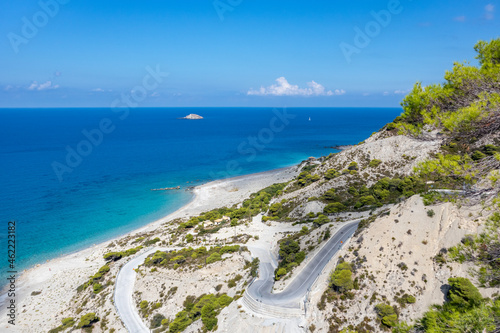Driving serpentine steep road to Gialos pebble beach with turquoise water and clear blue sky, Lefkada island, Ionian sea coast, Greece. Sunny summer scenic day trip