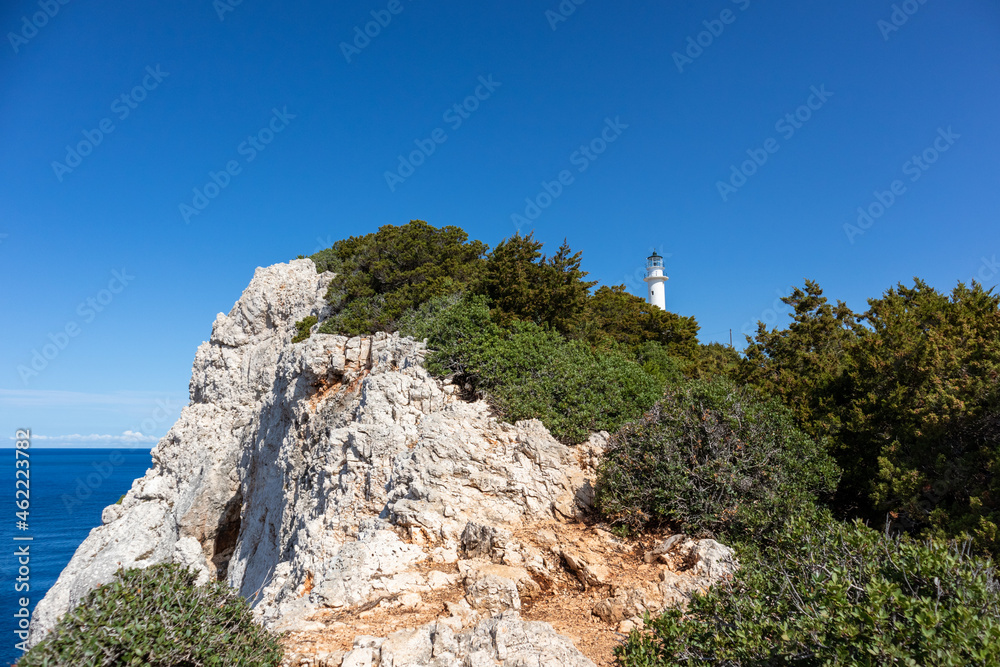 Ionian sea island steep rocky cliffs with lighthouse hidden in greenery on a bright clear blue sky in Greece. Scenic travel destination. Lefkada island.