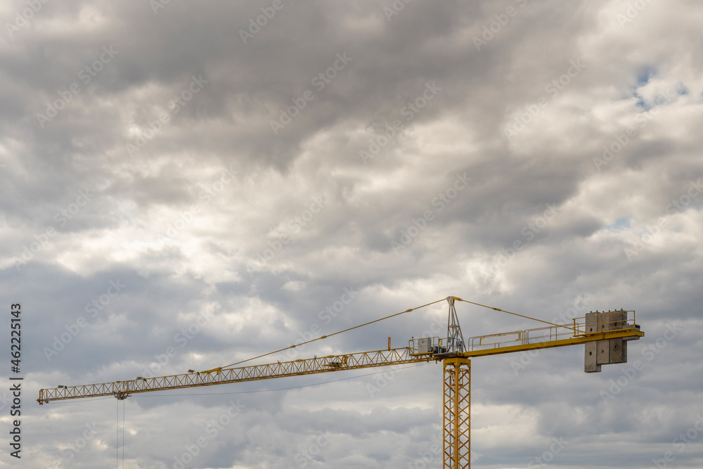 yellow building construction crane with counterweights on a cloud filled day