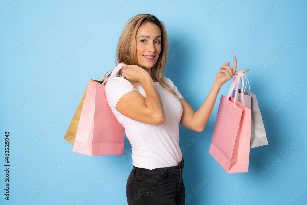 beautiful attractive smiling woman in white t-shirt and jeans holding shopping bags posing on blue isolated beautiful attractive smiling woman in white t-shirt and jeans holding shopping bags posing on blue isolated